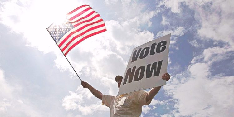 一位美國民眾舉著國旗與標語「VOTE NOW」。（Getty Images）